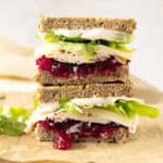 Stack of two halves of turkey cranberry lettuce sandwich on a beige paper.
