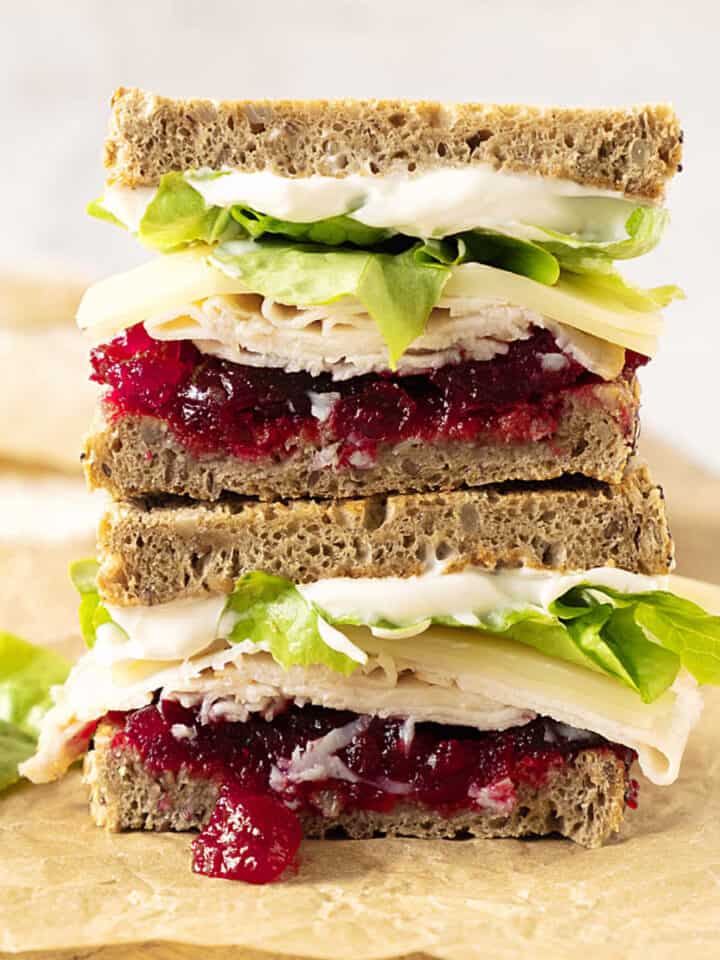 Stack of two halves of turkey cranberry lettuce sandwich on a beige paper.