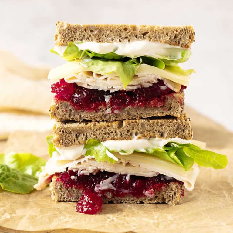 Stack of two halves of turkey cranberry lettuce sandwich on a beige paper.
