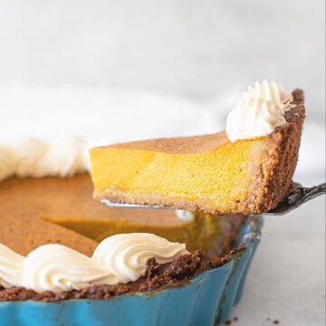 Pumpkin custard pie slice being lifted with a cake server from a teal pan. Light grey background.
