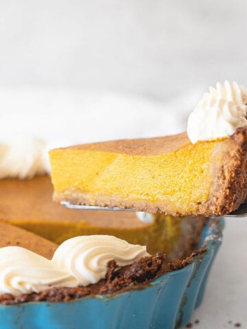 Pumpkin custard pie slice being lifted with a cake server from a teal pan. Light grey background.