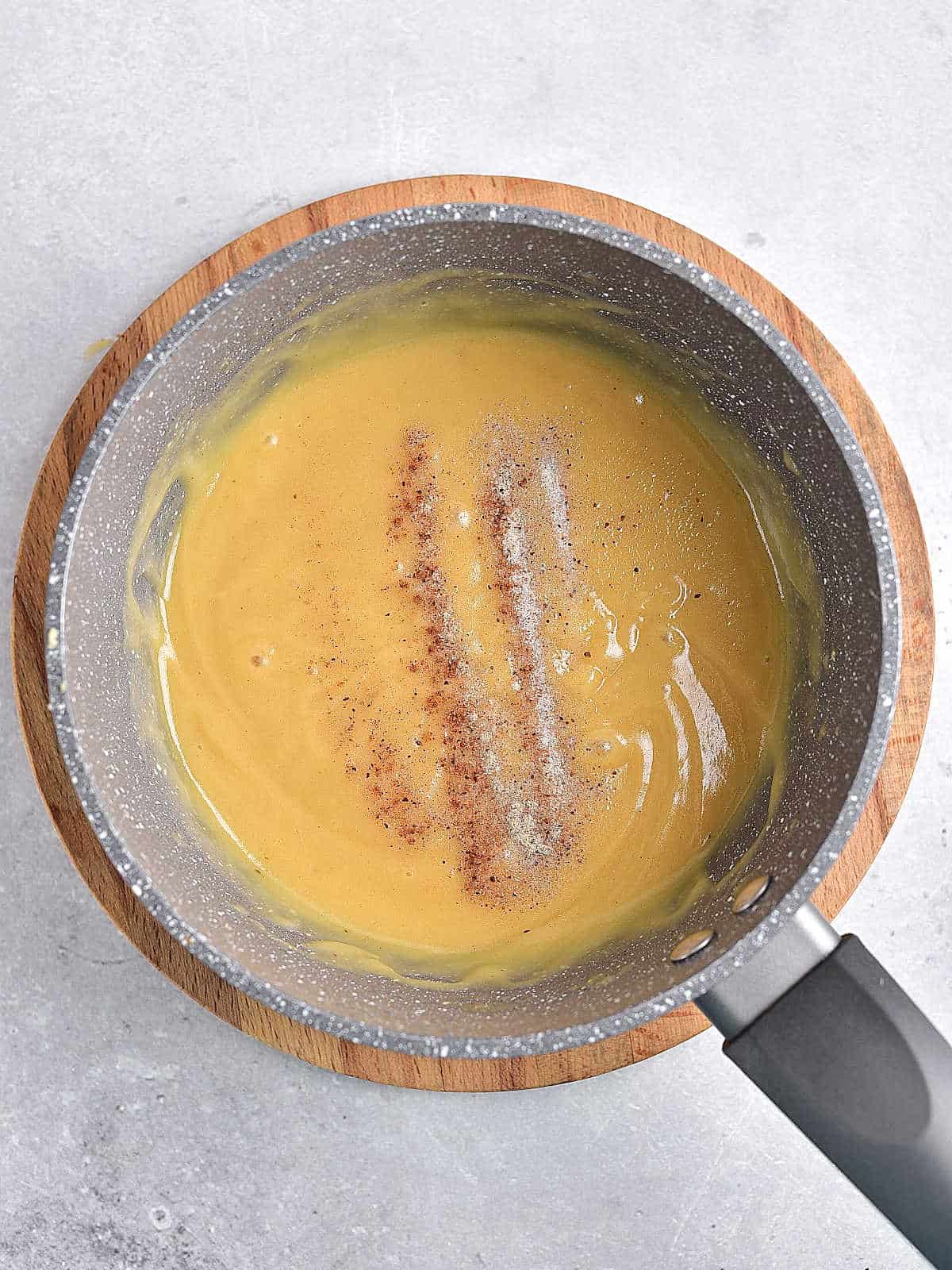 Light gray surface with saucepan containing gravy sprikled with spices.