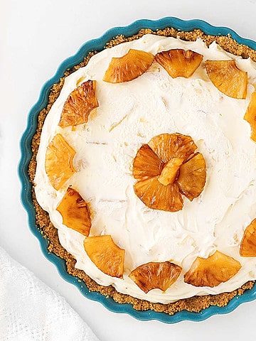 Teal dish on white surface with pineapple pie decorated with caramelized pieces. Top view.