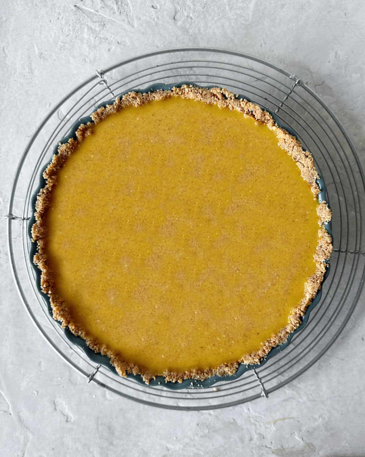 Top view of pumpkin custard pie before baking on a wire rack. Light grey surface.