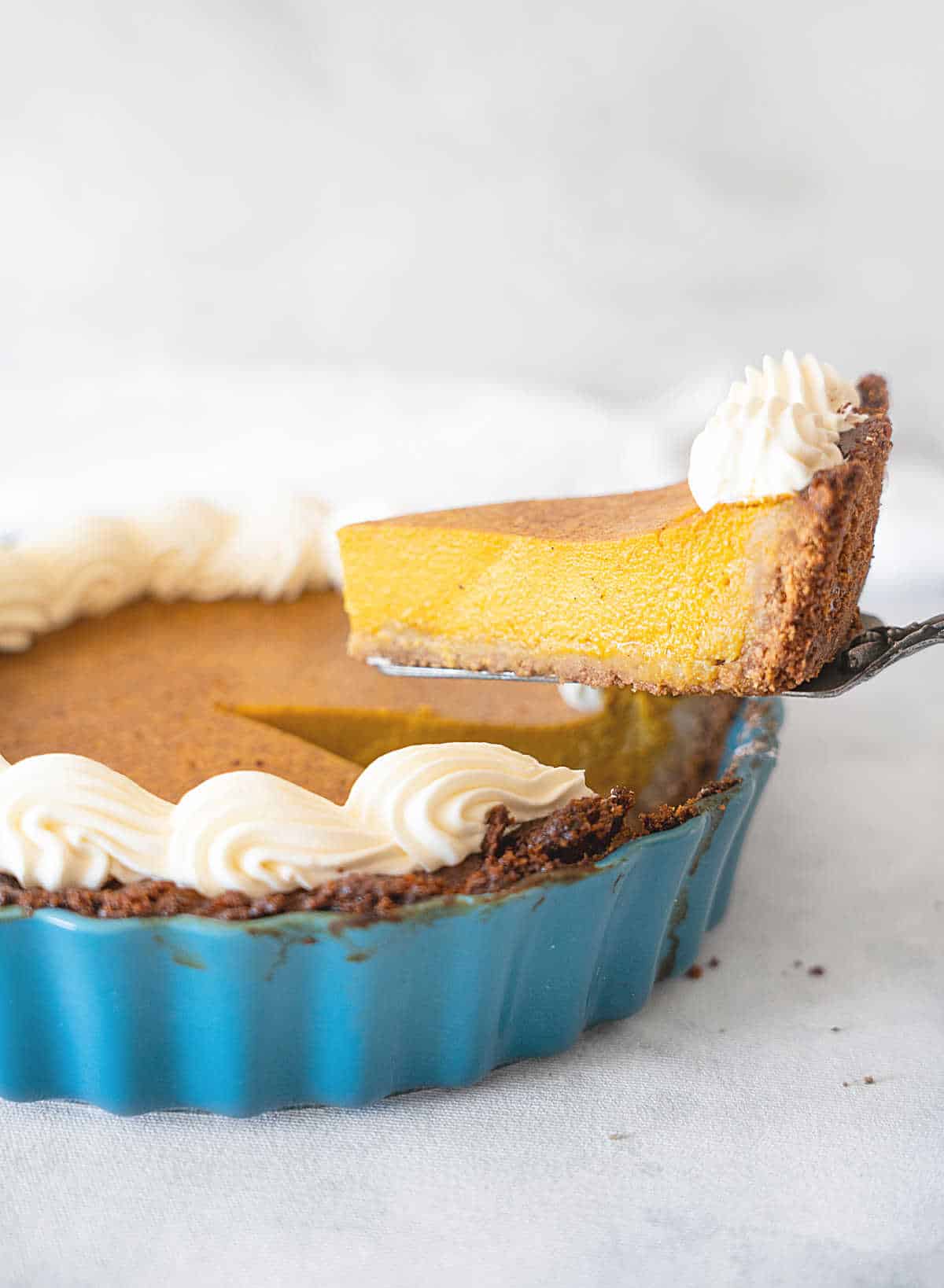 Lifting a slice of pumpkin pie from a teal ceramic pan. Light grey background. 