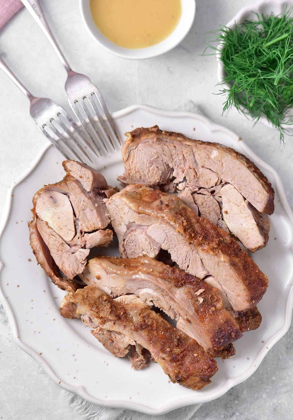 White plate with turkey thigh sliced. Silver forks, white surface, fresh dill.