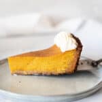 Grey white background and plate with slice of pumpkin custard pie with whipped cream.
