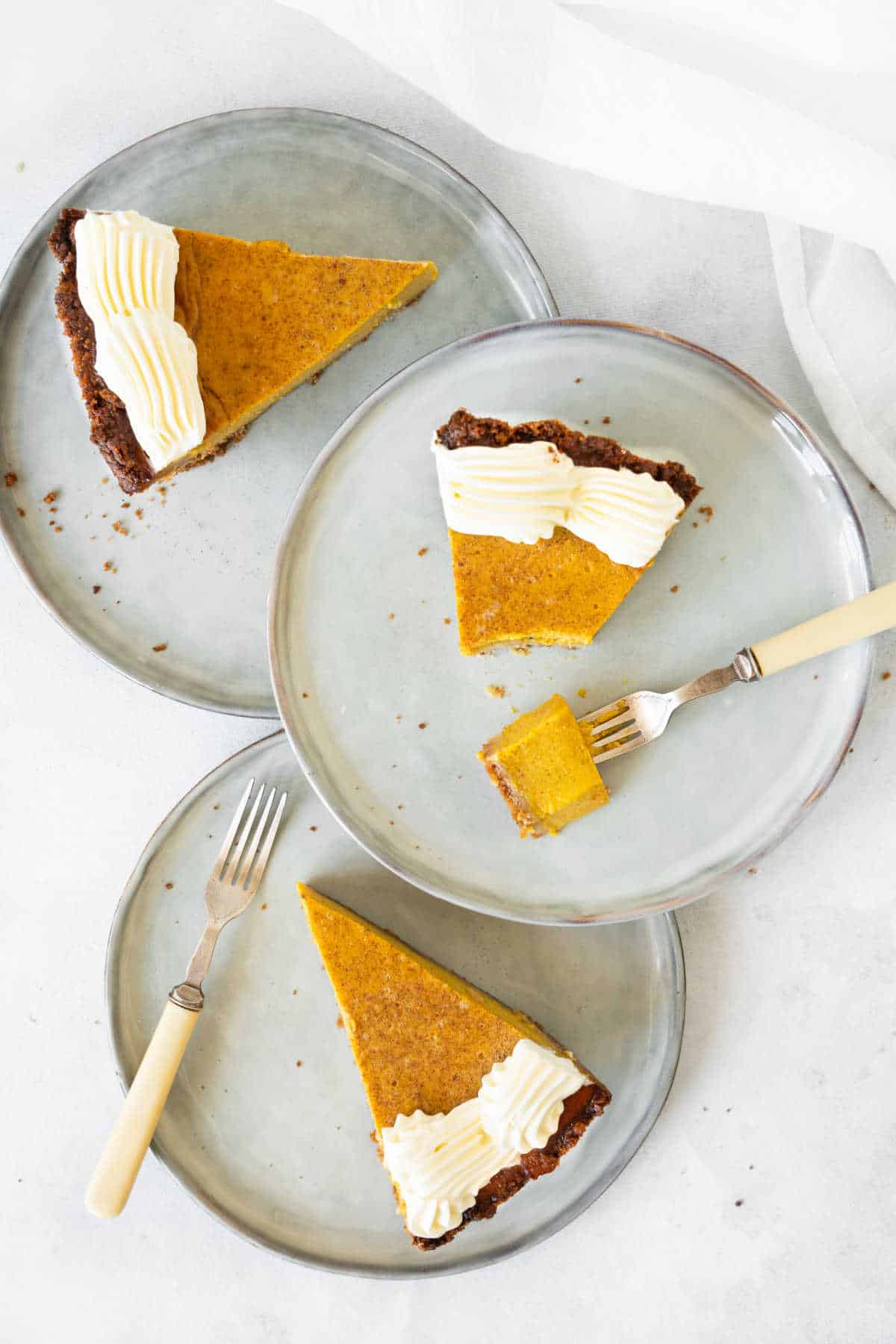 Three ovelapping grey plates with slices of pumpkin pie with whipped cream. Top view. White background. 