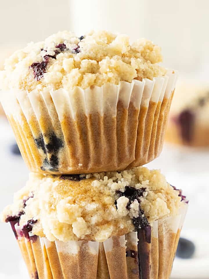 Partial view of stack of muffins with blueberries and crumb topping. Beige white background.