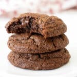 Three chocolate cookies stacked. Top one is bitten. White and red background.