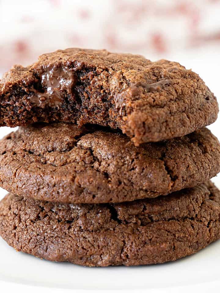 Three chocolate cookies stacked. Top one is bitten. White and red background.