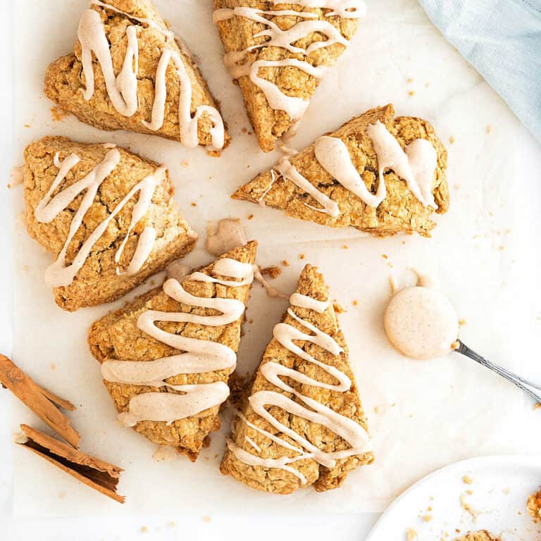 White surface with several triangles of glazed cinnamon scones. Spoon and cinnamon sticks.