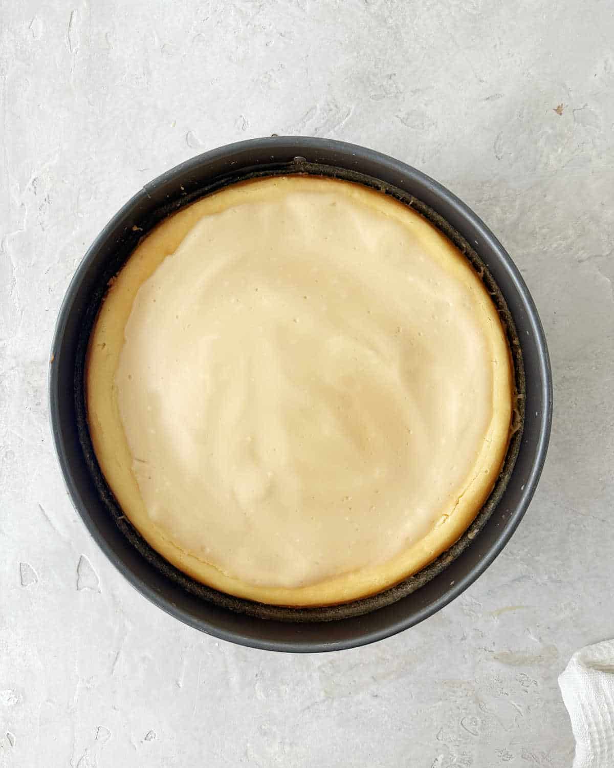 Baked Baileys cheesecake with sour cream topping on a metal pan. Light grey surface.