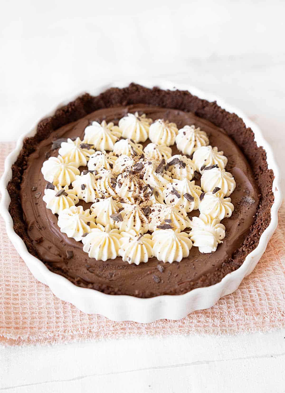 Whole chocolate cheesecake pie with crem on a white dish on a pink cloth. White background. 