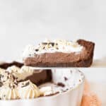 Close up slice of chocolate cream cheese pie being lifted from the white pie dish. Light grey background.