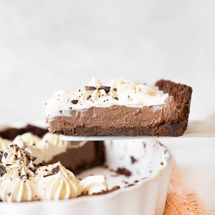 Close up slice of chocolate cream cheese pie being lifted from the white pie dish. Light grey background.