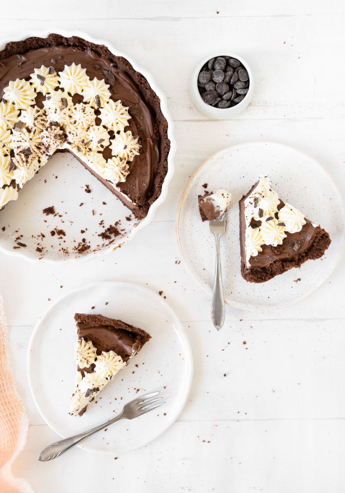 Top view of chocolate cream tart on a white dish. Slices on white plates with silver forks. White surface. 