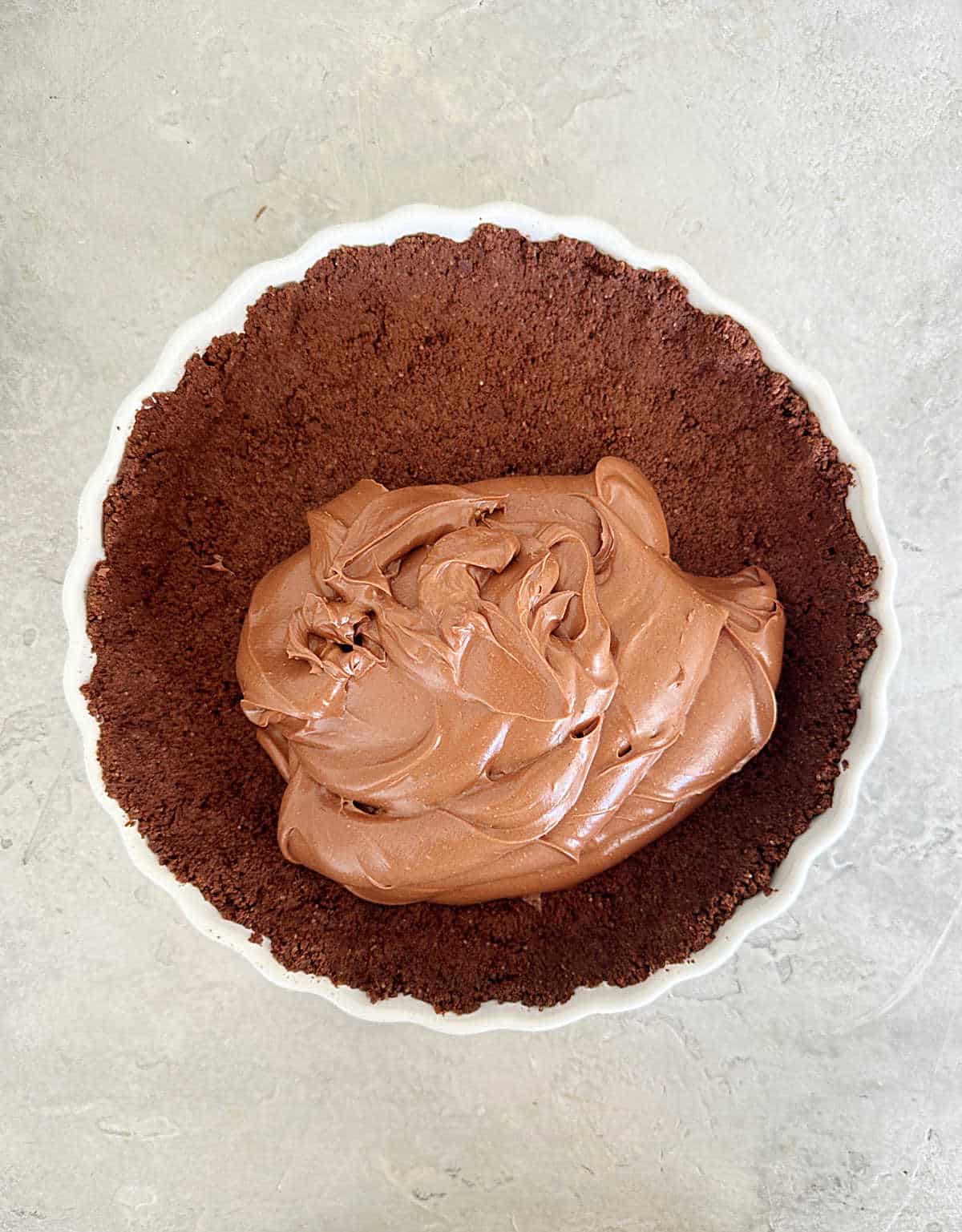 Chocolate filling in a chocolate crust on a white dish. Light grey surface.