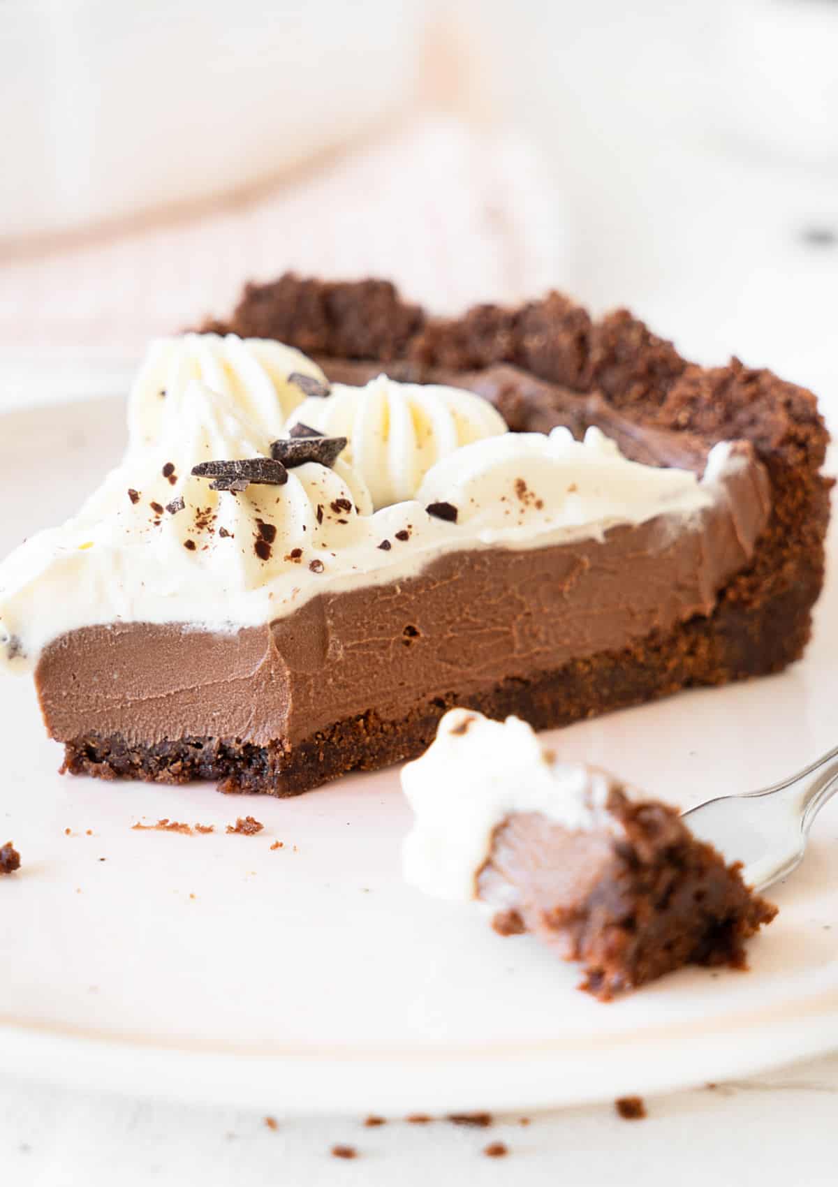 Eaten slice of chocolate cream cheese pie on a pinkish plate. Bite in a fork. White and pink background. 