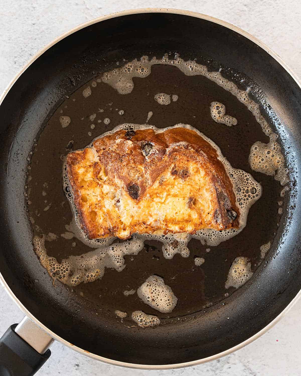 Balck skillet with panettone French toast piece being cooked.