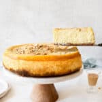 A slice of Baileys cheesecake being lifted from the cake stand. White surface and light grey background.