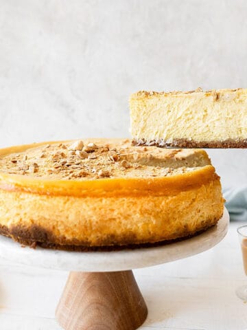 A slice of Baileys cheesecake being lifted from the cake stand. White surface and light grey background.