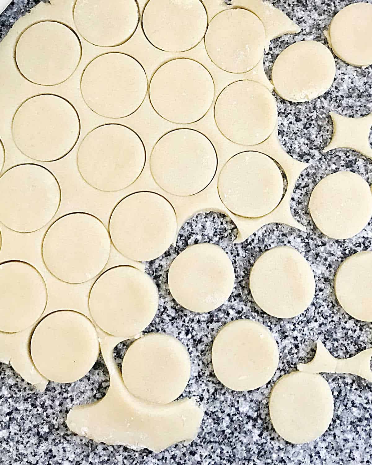 Grey granite surface with rolled shortbread dough and cut round cookies.
