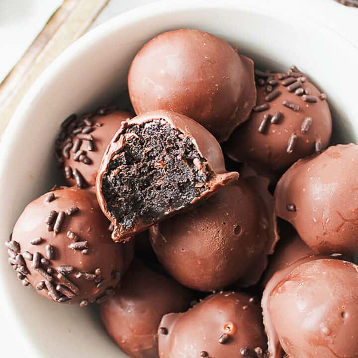 Bitten chocolate-covered Oreo truffle over several whole more in a white bowl.