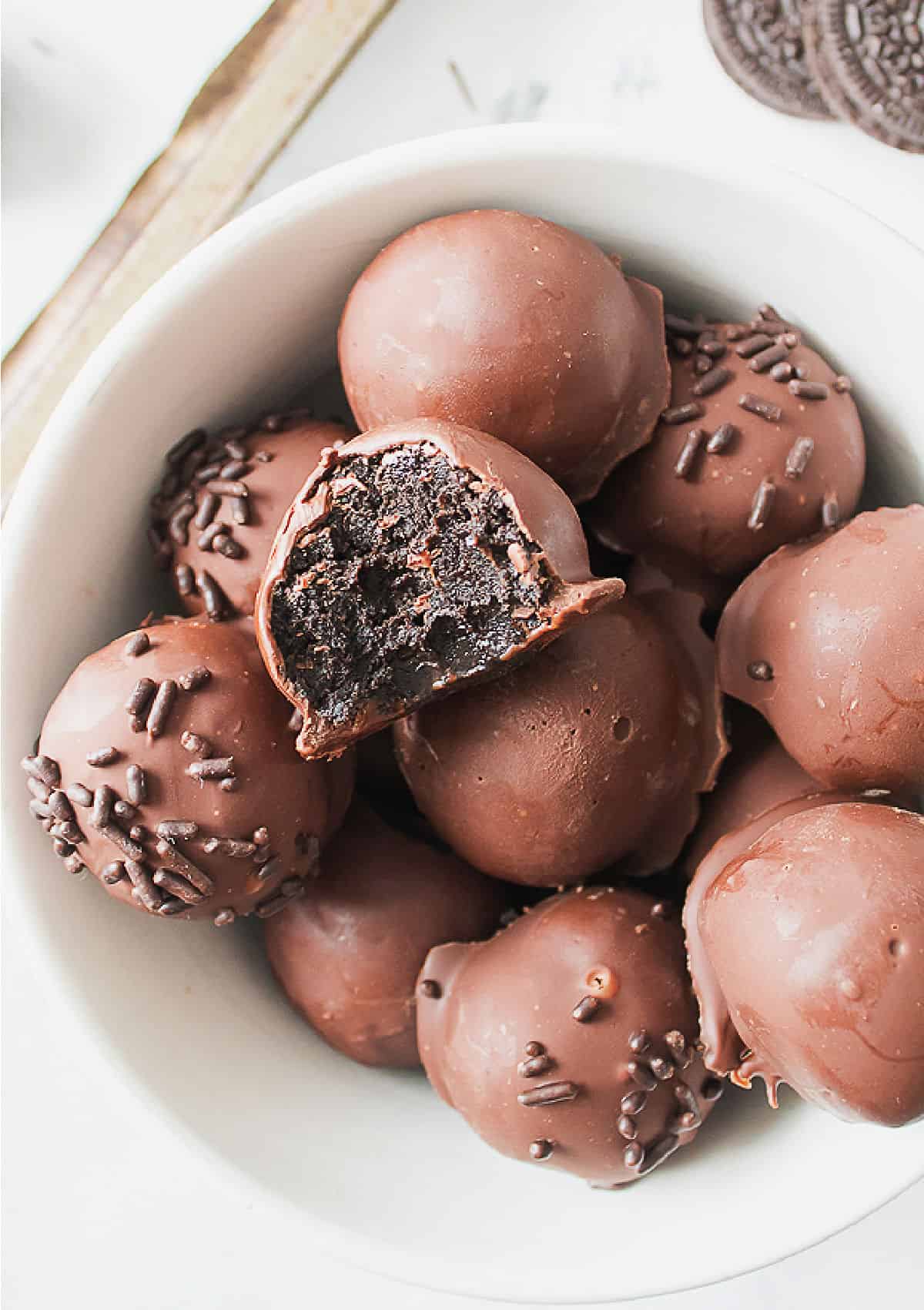 White bowl with whole and bitten chocolate-covered Oreo truffles. 