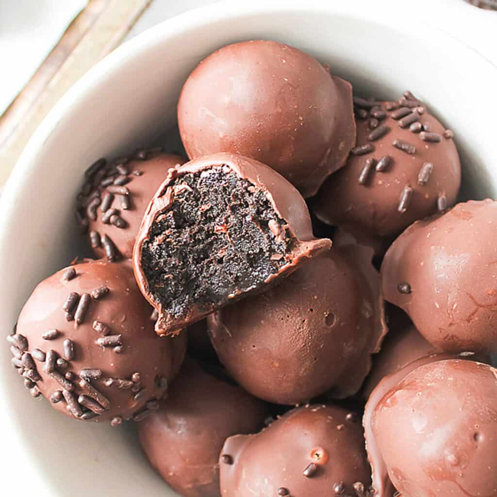 Bitten chocolate-covered Oreo truffle over several whole more in a white bowl.