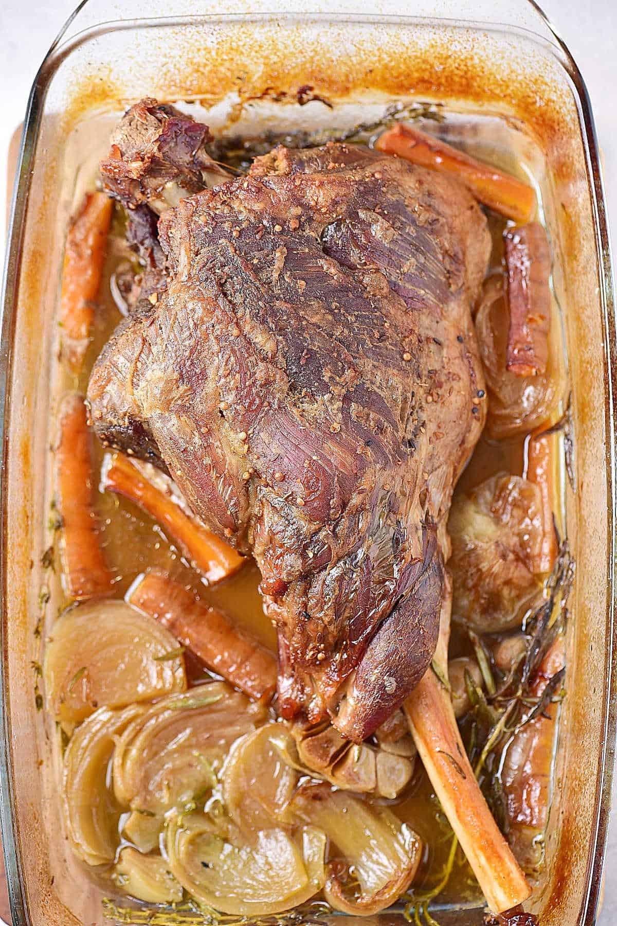 Oven roasted leg of lamb with carrots and onions in a glass dish.