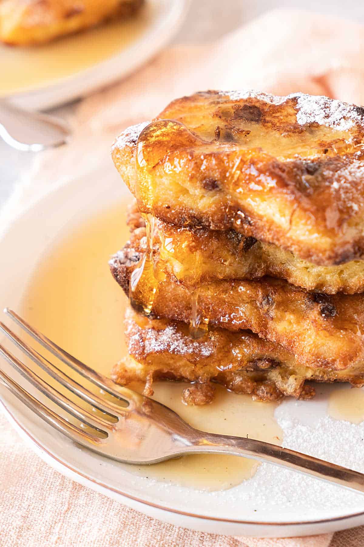 Stack of panettone French toast dripping syrup on a white plate with a silver fork.