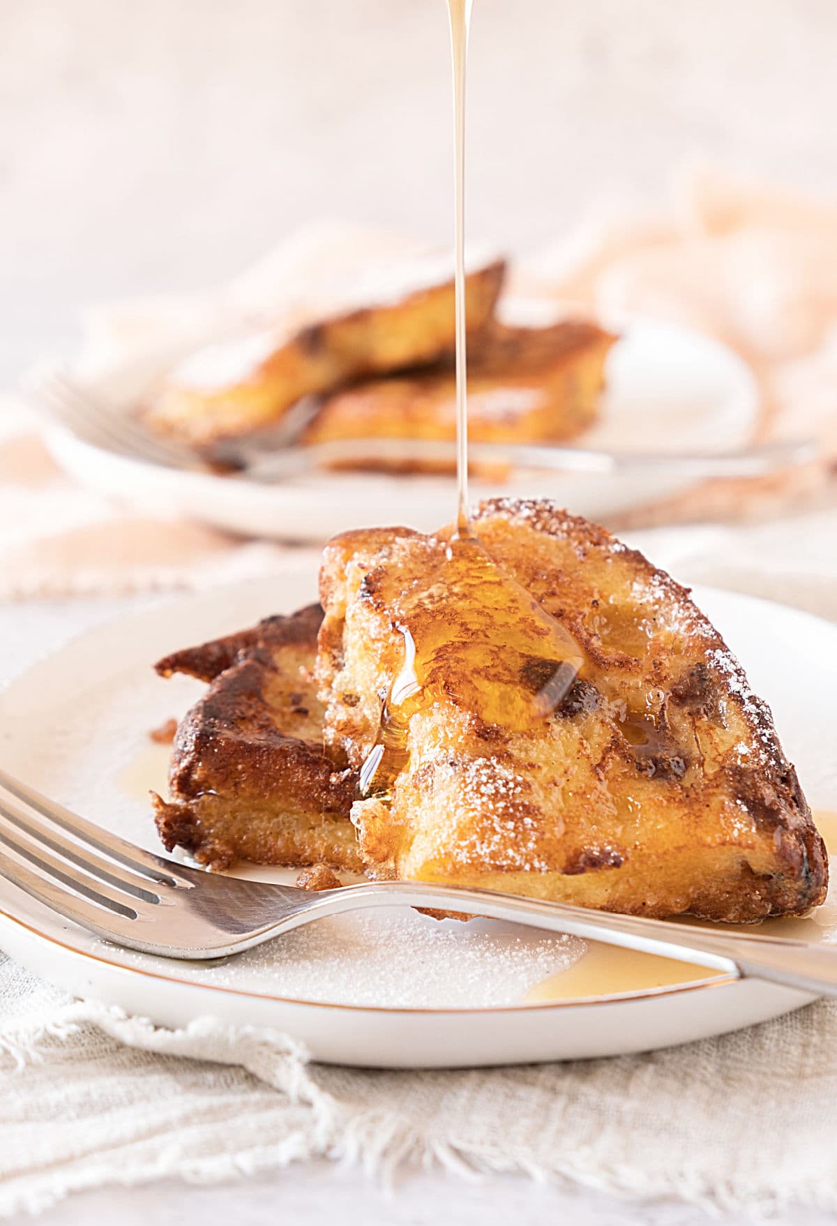 Drizzling maple syrup of two slices of panettone French toast on a white plate.