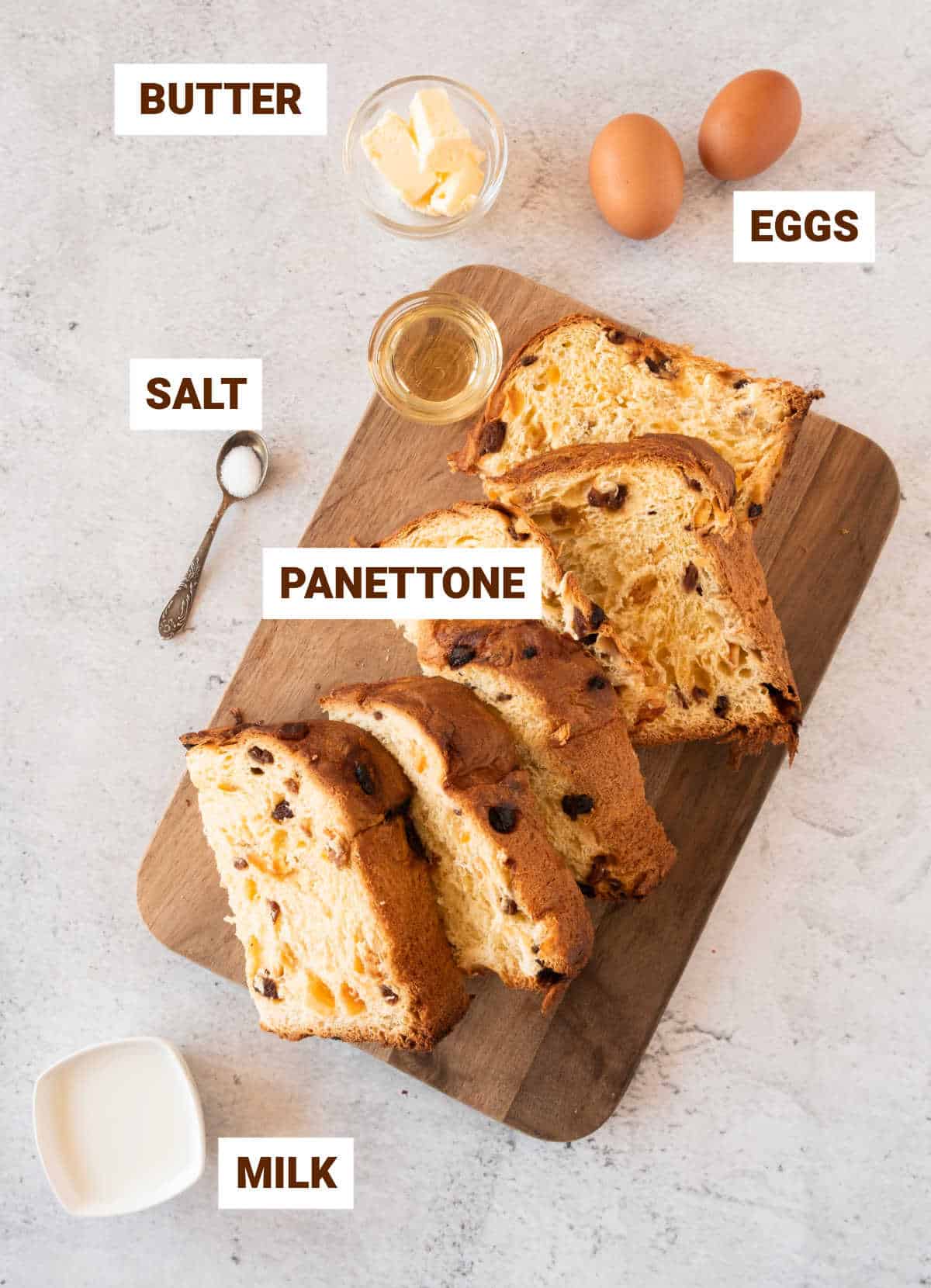 Wooden board on a gray surface with slices of panettone, eggs, butter, milk and salt.