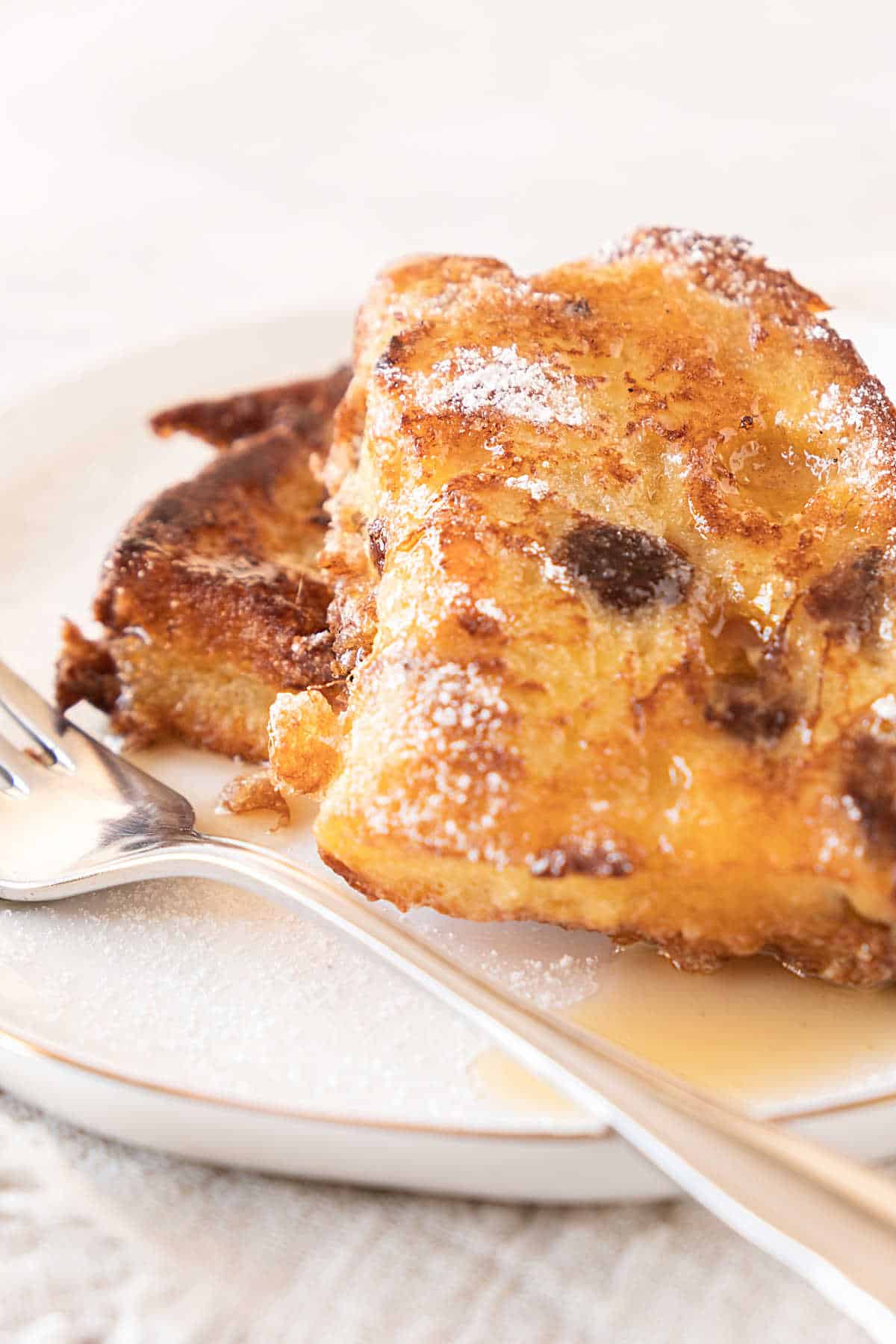 Close up of two slices of panettone French toast on a white plate. Silver fork and white background. 