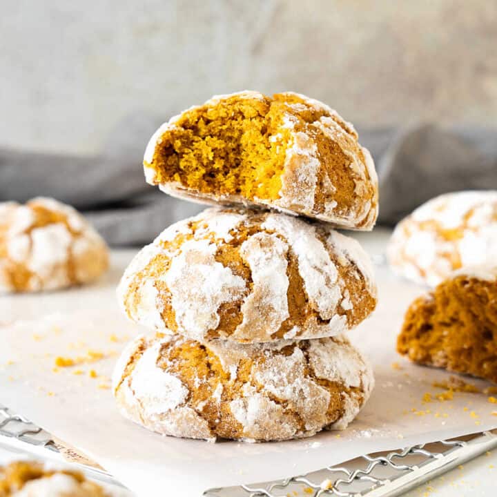 Stack of three pumpkin crinkle cookies on white paper. Top one is bitten. Grey background.