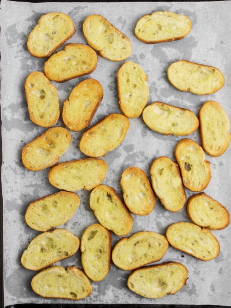 Baked baguette slices with oil on parchment paper. Top view.