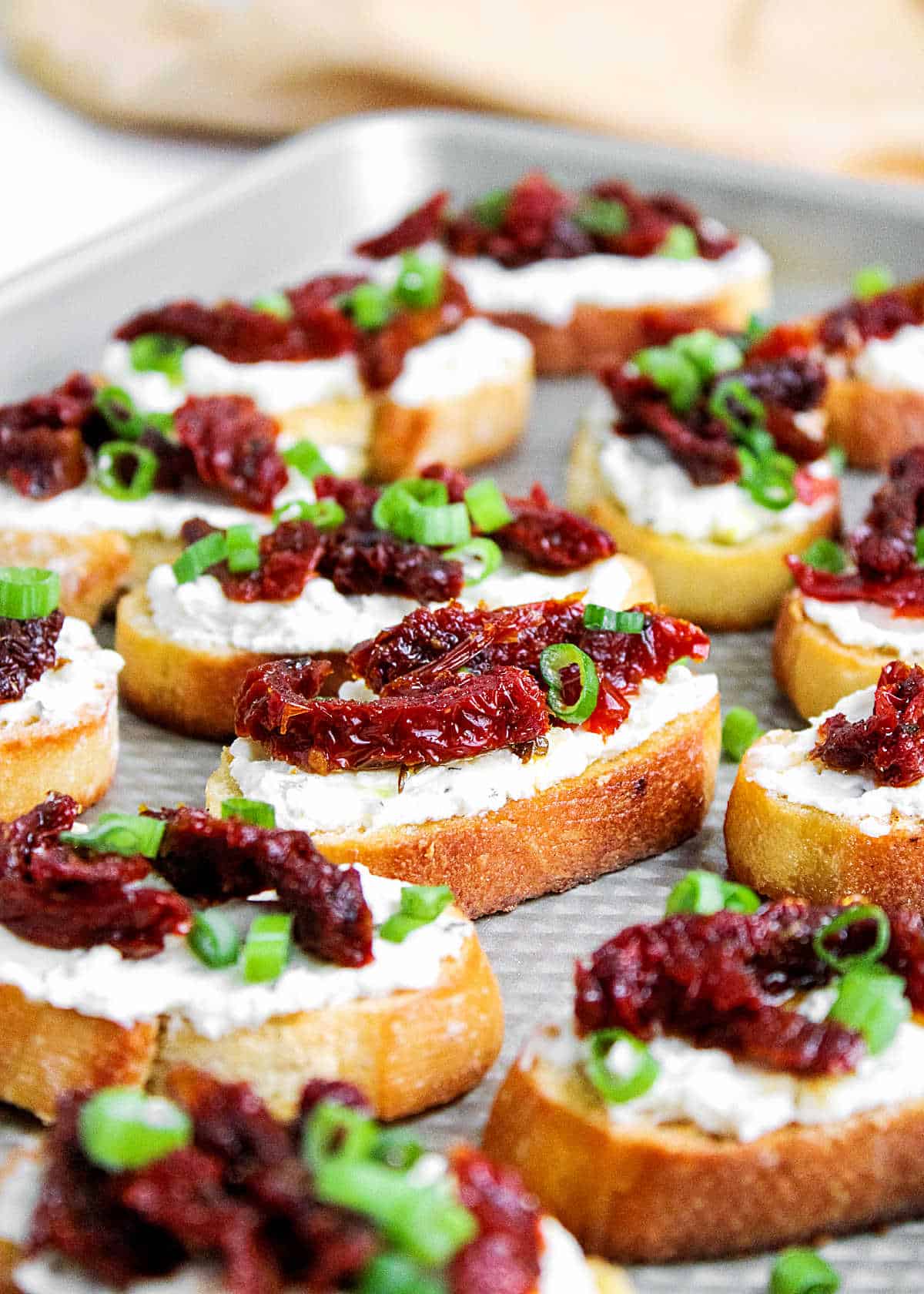 Several dried tomato, ricotta and chive bruschettas on a metal pan. 