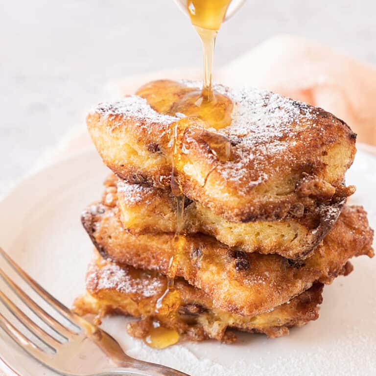 A stack of panettone French toast drizzling syrup on a white plate. Light gray background.