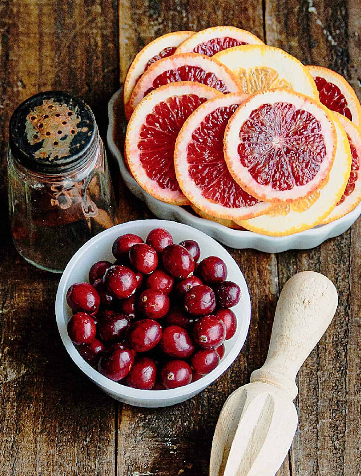 Bowls with cranberries and blood orange slices on a wooden surface. Citrus wooden hand juicer.
