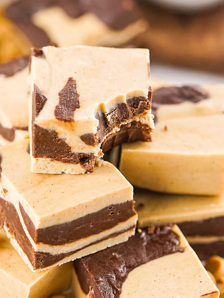 Close up of pile of chocolate peanut butter marbled fudge squares. Top one is bitten.