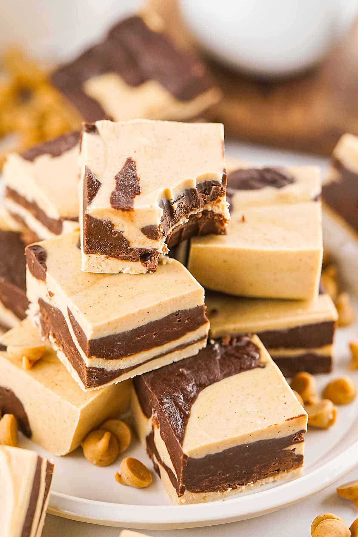 A pile of chocolate peanut butter marbled fudge squares on a white plate. Top one is bitten. 