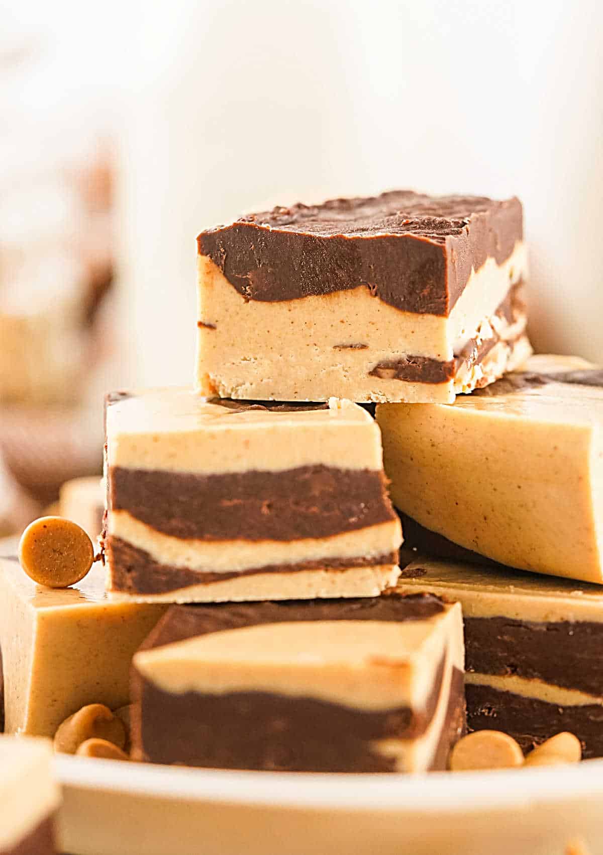 Pile of marbled peanut butter chocolate fudge squares on a beige plate. White background. 