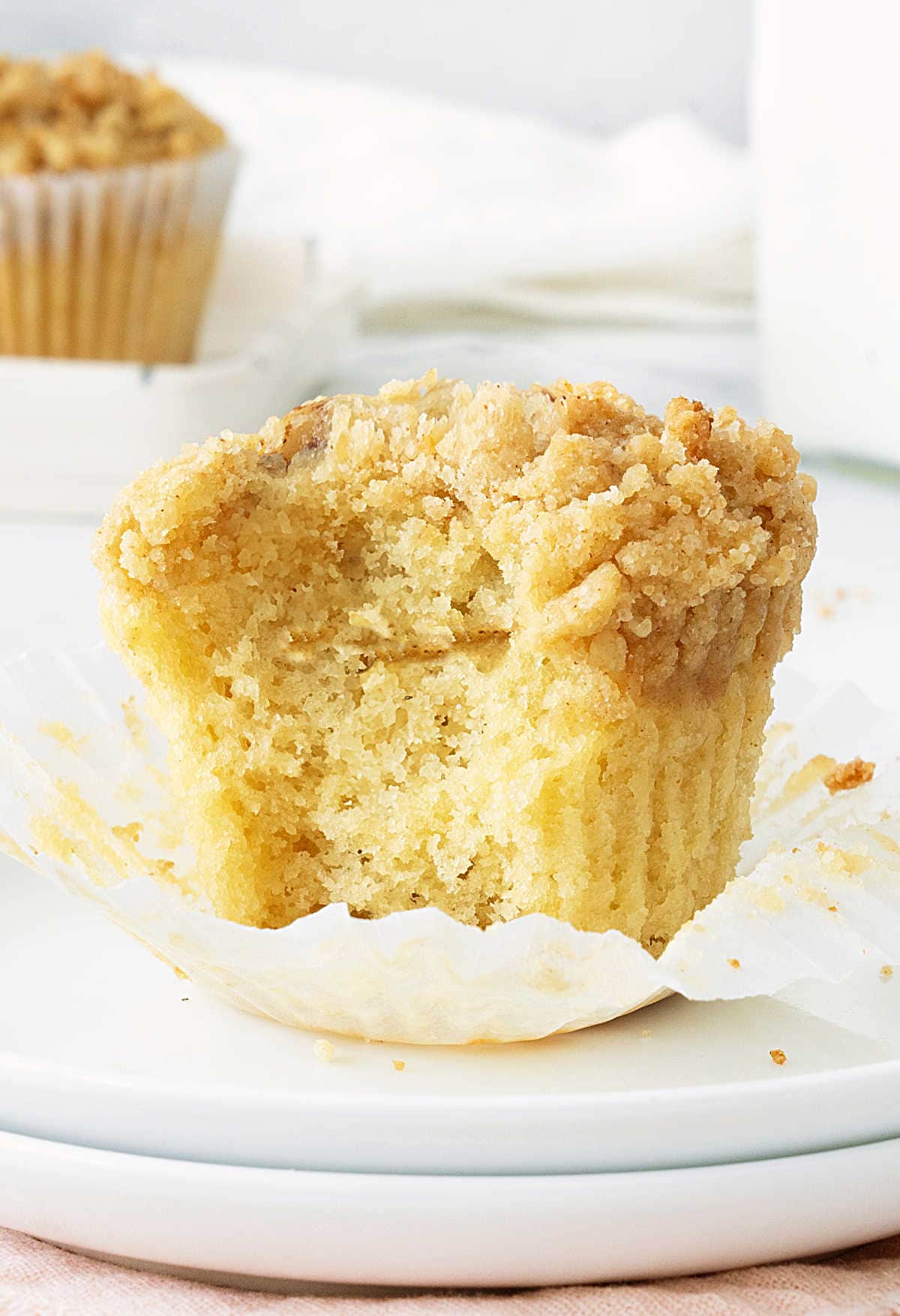 Bitten cinnamon crumb muffin on an opened paper liner on a white plate.