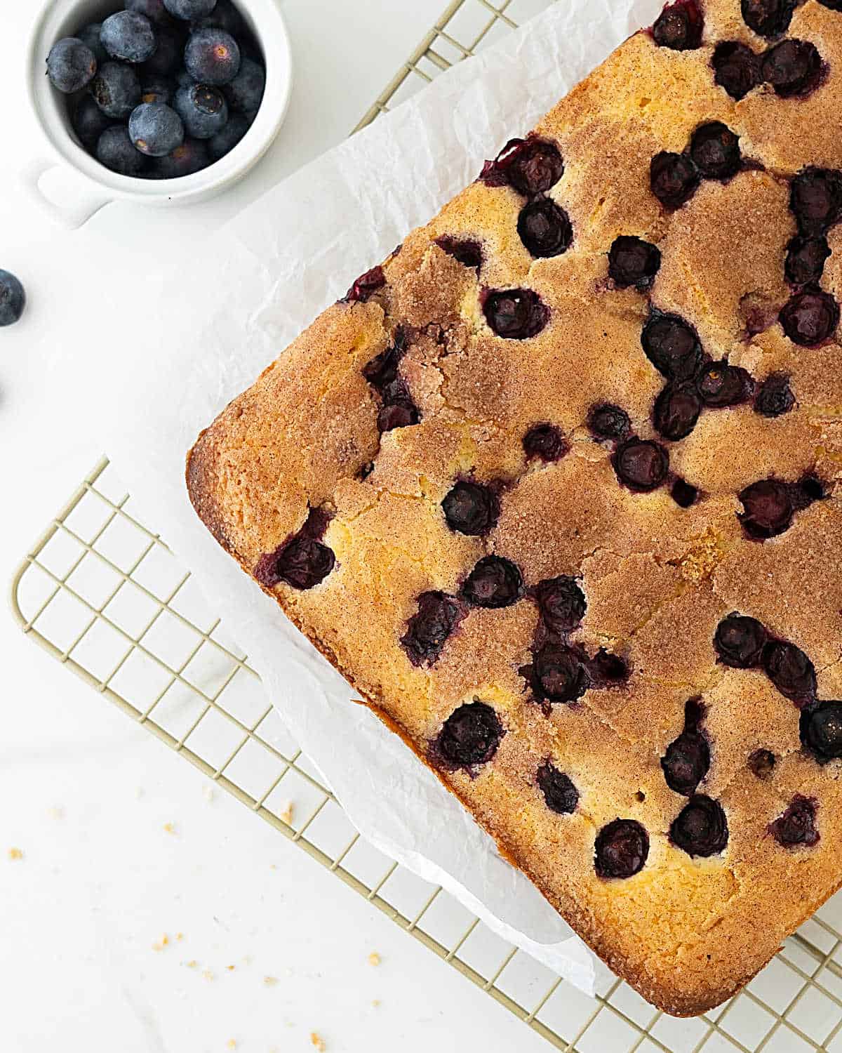 Baked blueberry coffee cake on a wire rack. White surface. Bowl of blueberries.