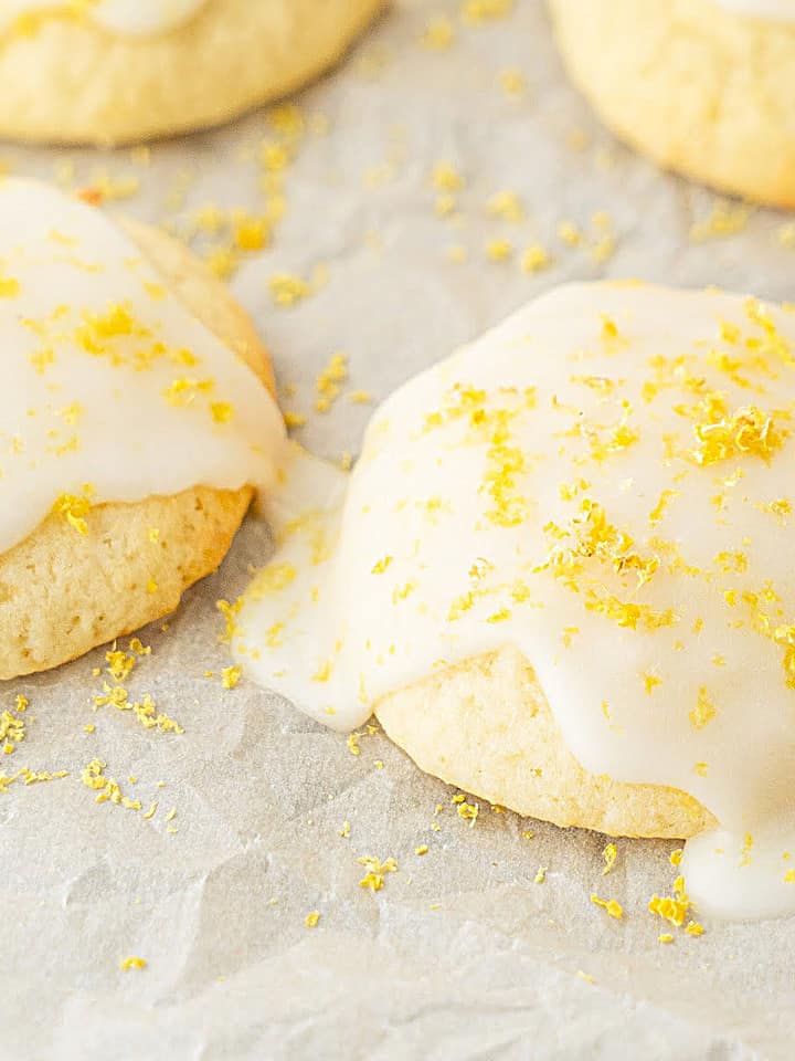 Glazed ricotta cookies with lemon zest on white parchment paper.