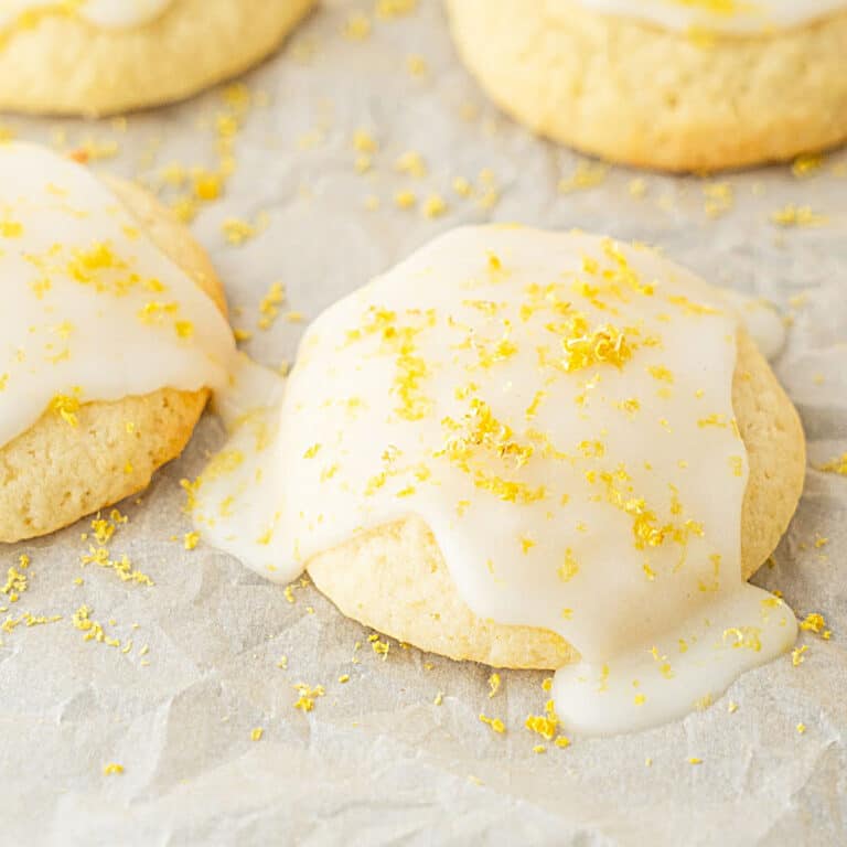 Glazed ricotta cookies with lemon zest on white parchment paper.