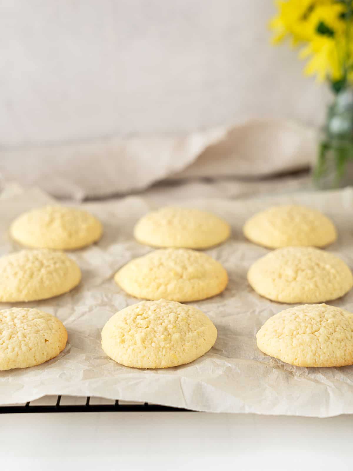 Plain baked ricotta cookies on white paper. Gray background, yellow flowers.