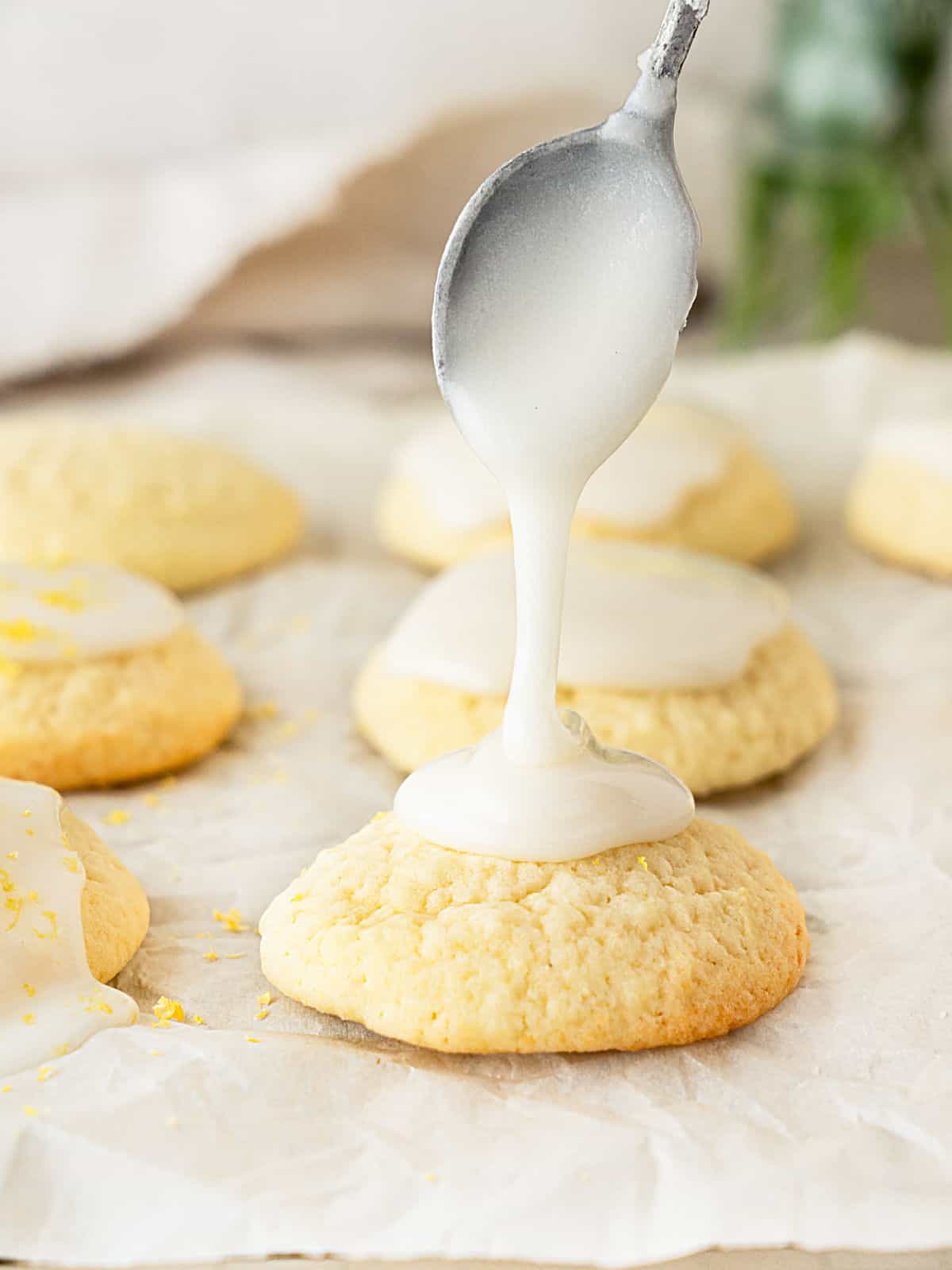 Glazing a ricotta cookie with a spoon. White parchment paper surface.