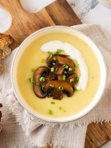 Potato, leek and mushroom soup in a white bowl on a beige linen. Wooden board, white marble, toast pieces.